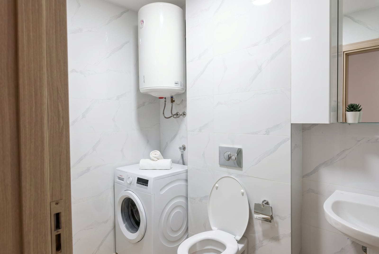 Modern bathroom in an apartment in Bečići, Montenegro: white marble-look tiles, washing machine, and water heater.
