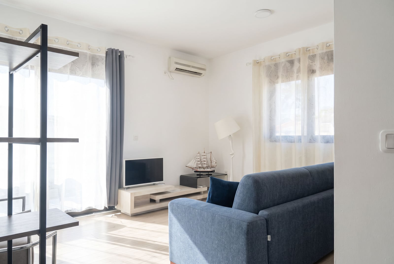 Bright living room with a blue sofa, TV area, and panoramic window in an apartment in Budva, Montenegro