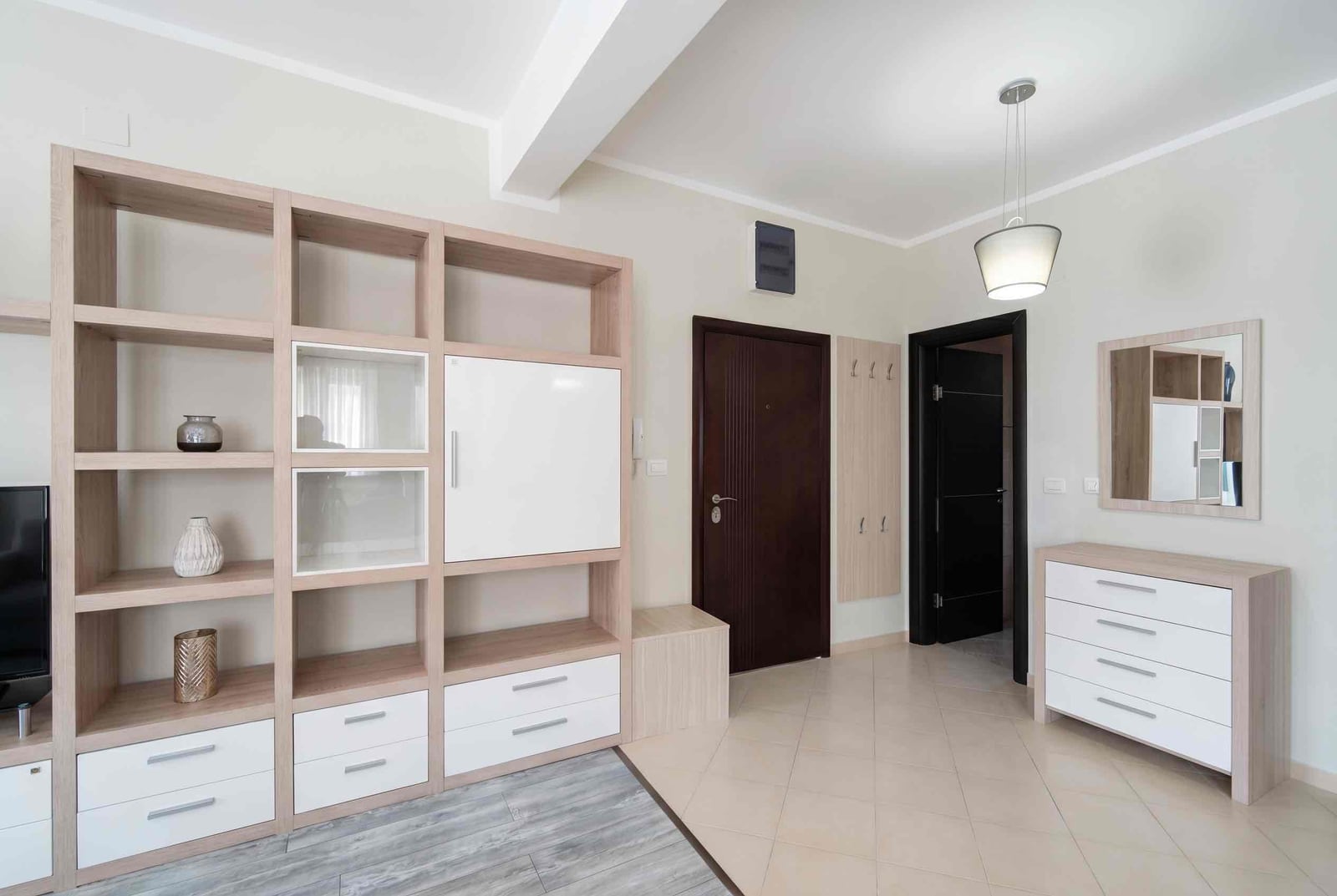 Living room interior in an apartment in Bečići, Montenegro: light-colored furniture, shelving unit, dresser with a mirror, and tiled flooring.