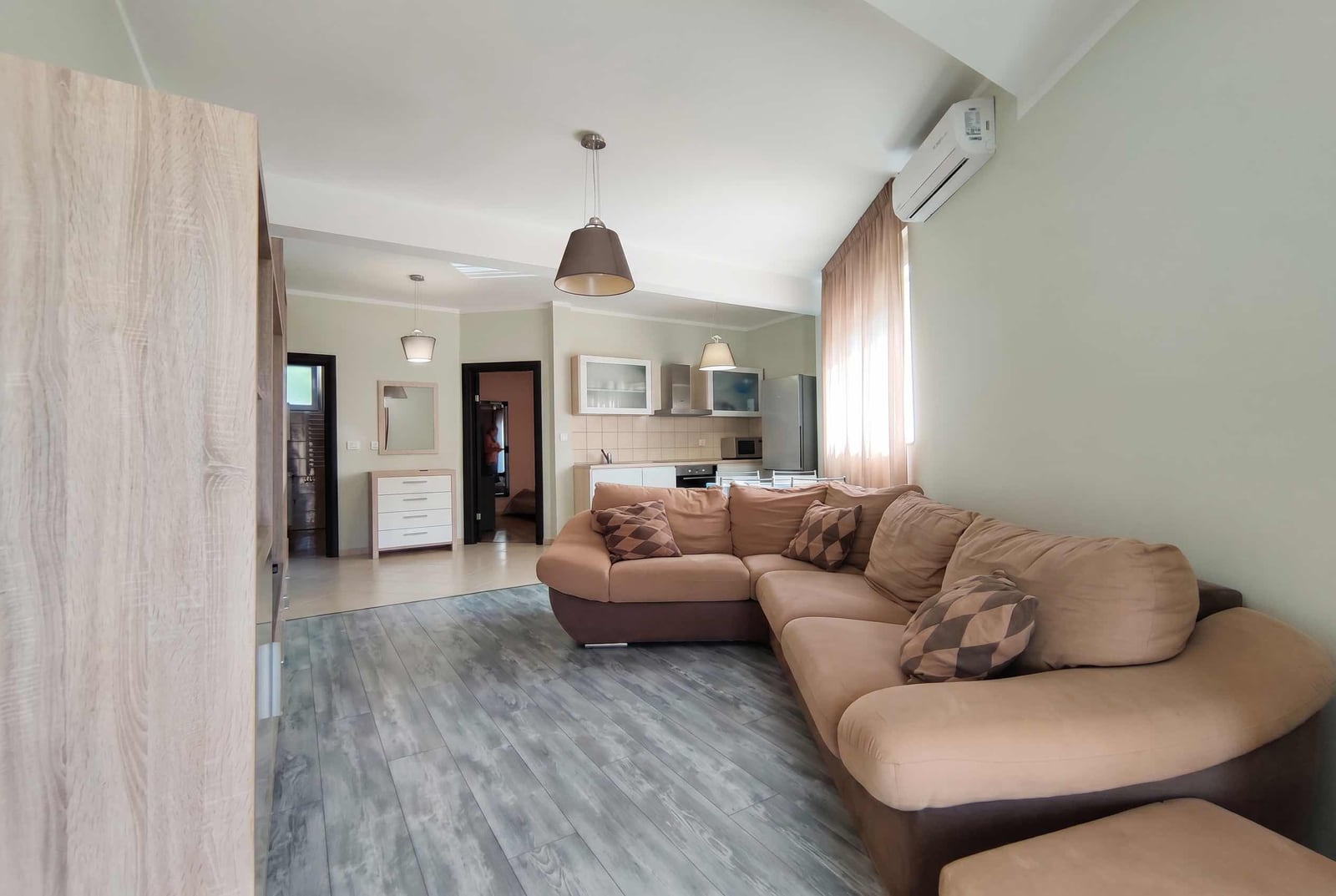 Living room with a sectional sofa and kitchen in a modern apartment, Bečići, Montenegro: bright interior, laminate flooring, air conditioning.