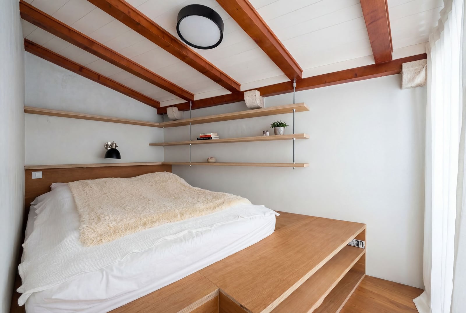 Bedroom in an apartment in Budva, Montenegro: a bed on a wooden platform, open shelves, and a beamed ceiling.