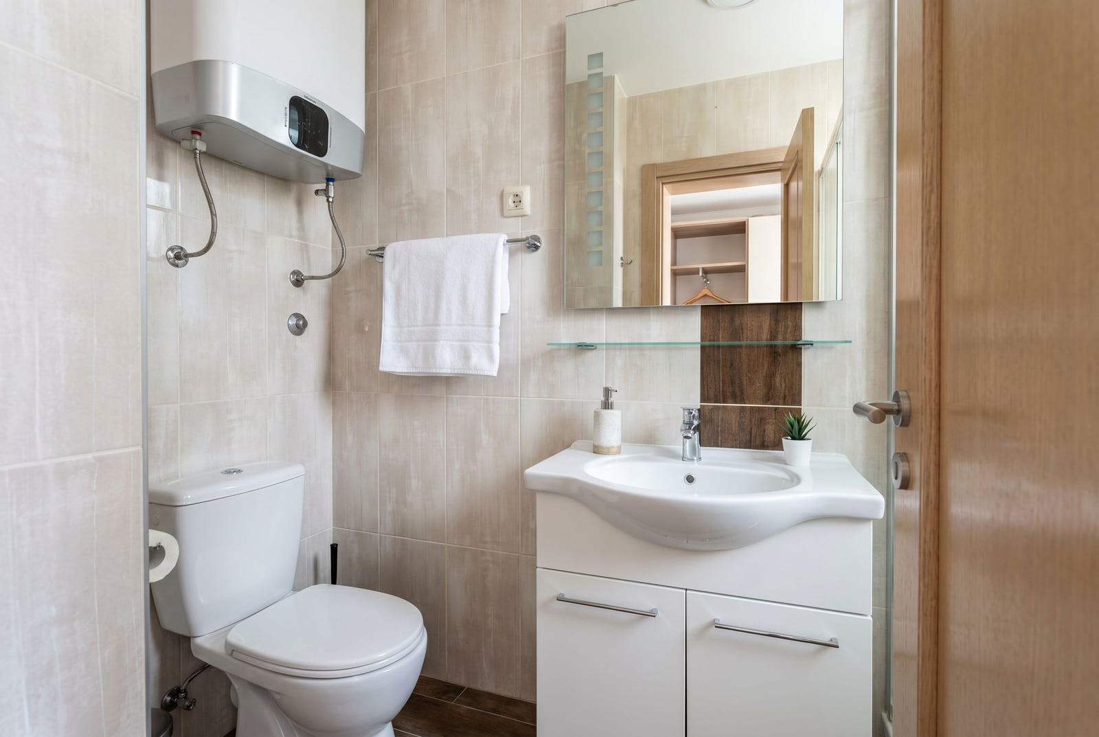 Modern bathroom in an apartment, Becici, Montenegro: white sanitary ware, water heater, and light-colored tiles.