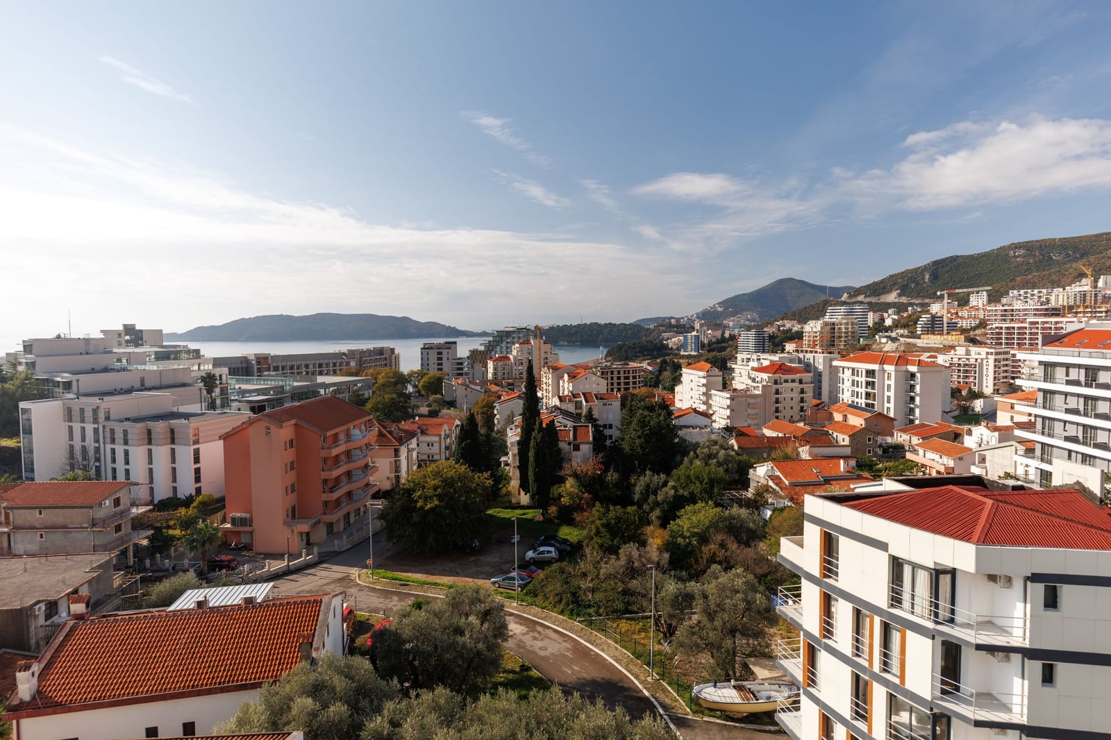 Panoramic view of the town of Bečići, Montenegro, featuring modern residential complexes, mountains, and the coastline.
