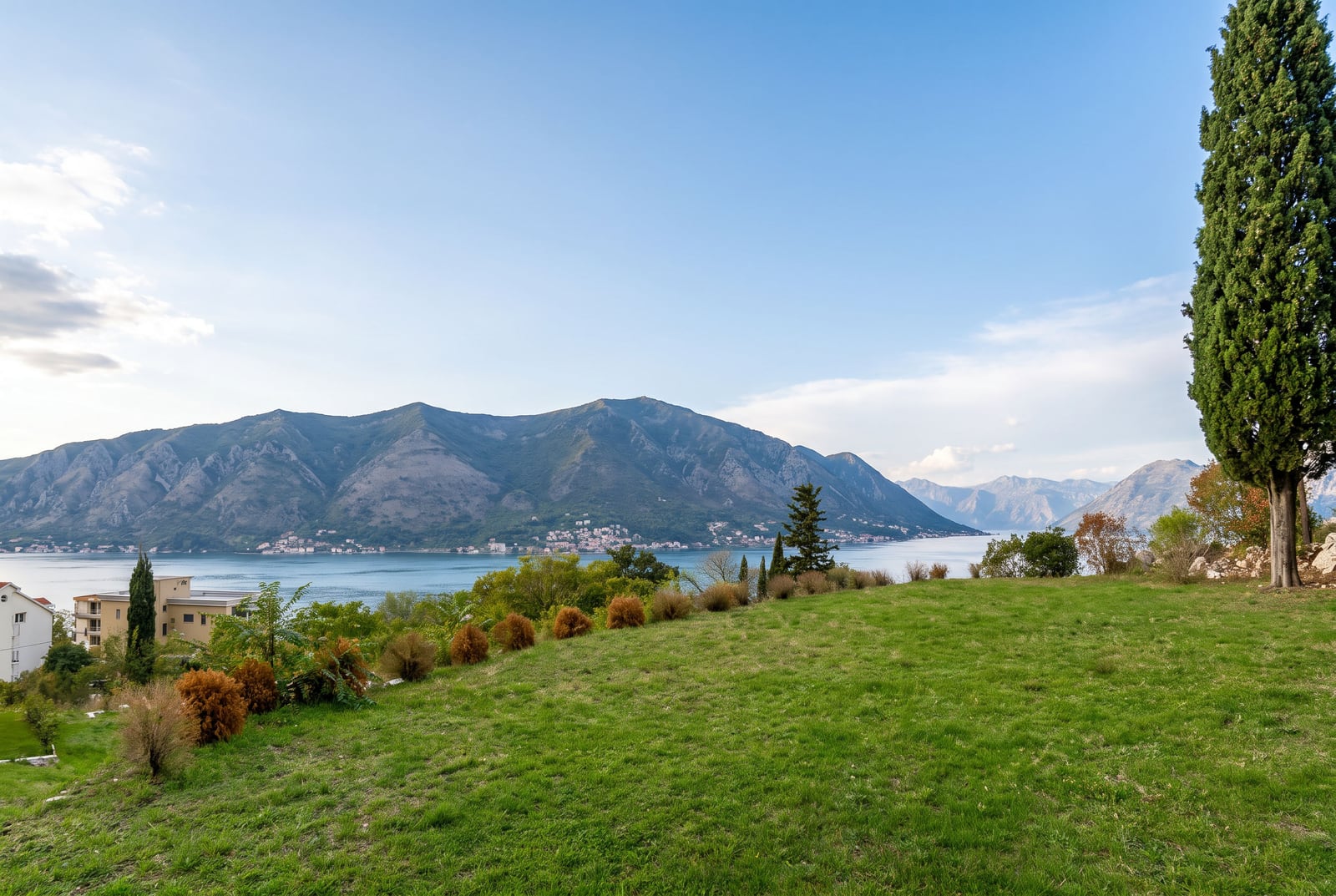 Panoramic view of water and mountains from a green grassy slope with trees.
