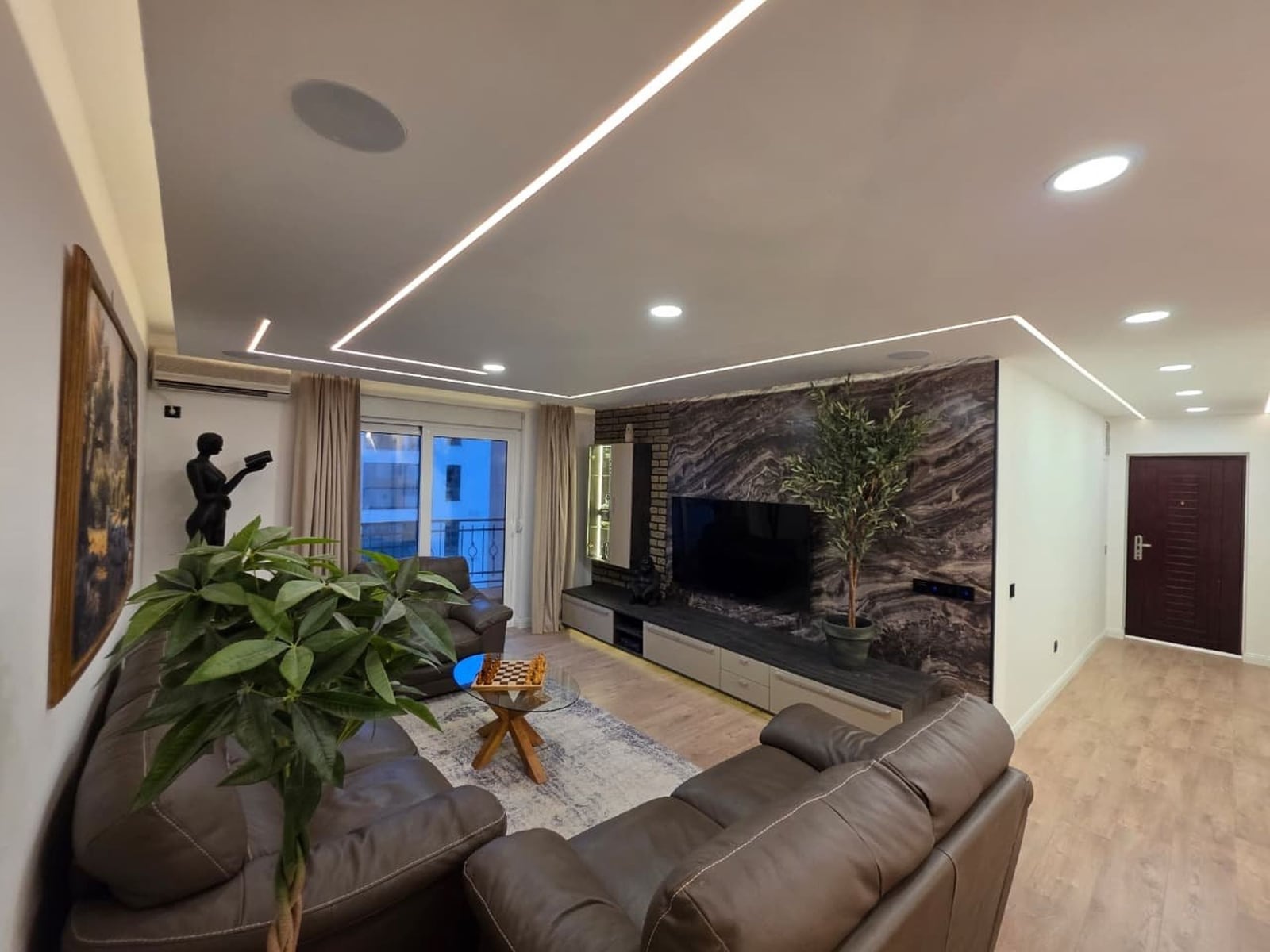 Modern living room in an apartment in Bečići, Montenegro: leather sofas, a TV area with marble finish, and LED lighting.