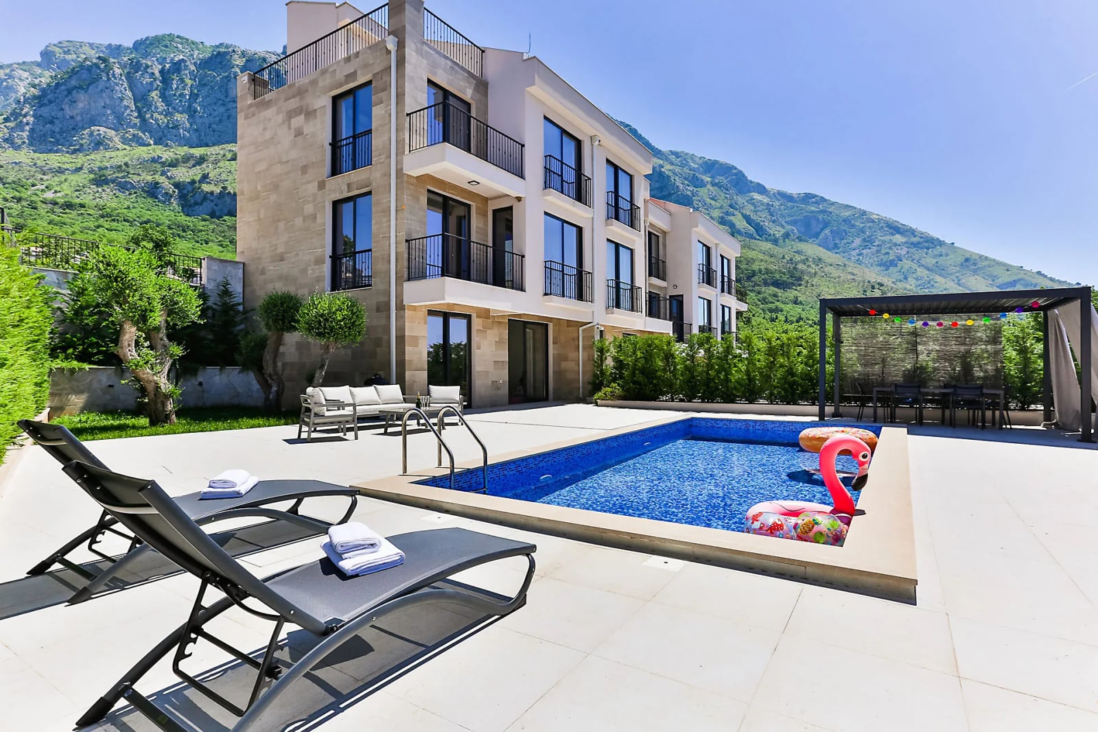 Modern villa with a swimming pool and sun loungers in Reževići, Montenegro, set against a backdrop of picturesque mountain scenery.