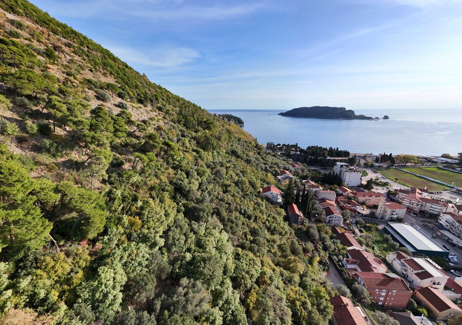 Panoramic sea view of St. Nicholas Island from a land plot in Budva, Montenegro, surrounded by hills and greenery.