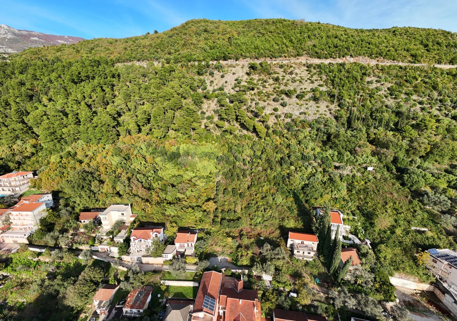 Land plot in Budva, Montenegro: aerial view of houses at the foot of a green hill with dense vegetation.