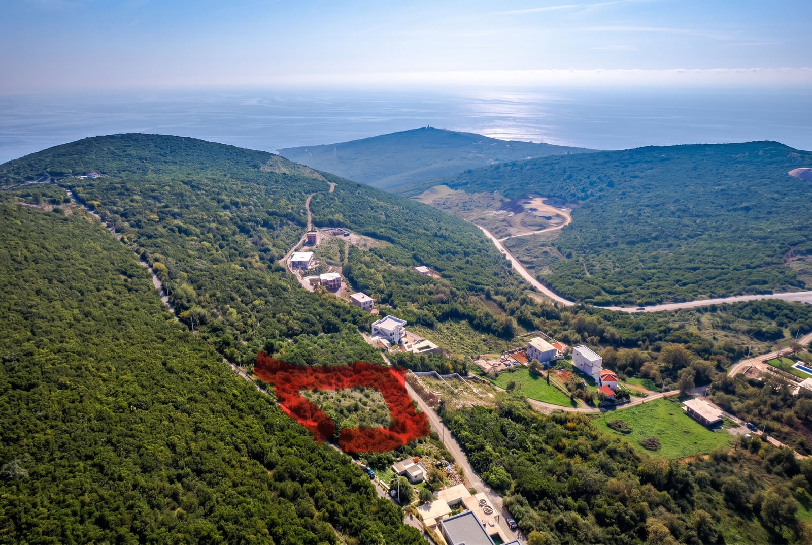 Land plot in Visnjevo, Budva, Montenegro: aerial view of the plot nestled among hills with a panoramic sea view.