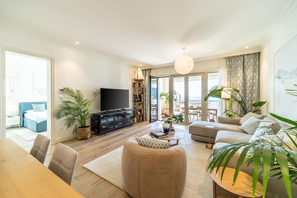 Bright living room with a terrace and sea view in an apartment, Luštica, Montenegro: modern furniture, decor, and plants.
