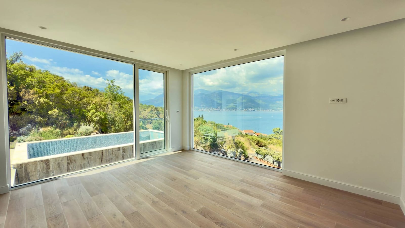 Living room with panoramic windows, sea view, and a pool at a villa in Krašići, Montenegro. Bright interior with parquet flooring.