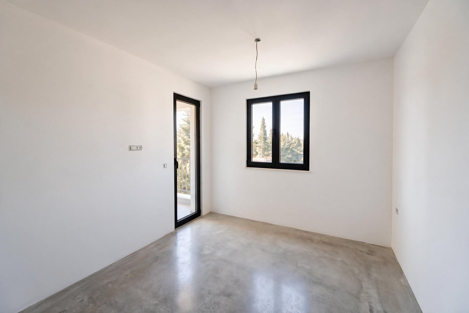 Empty room with white walls, concrete floor, window, and door leading to a balcony.