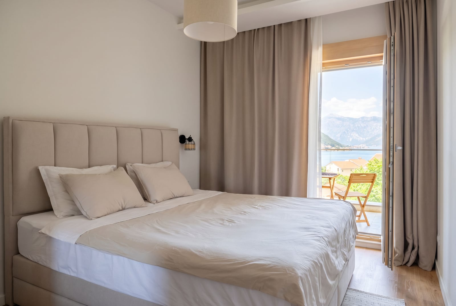 Bedroom in an apartment in Dobrota, Montenegro: double bed, light interior, and balcony with sea and mountain views.