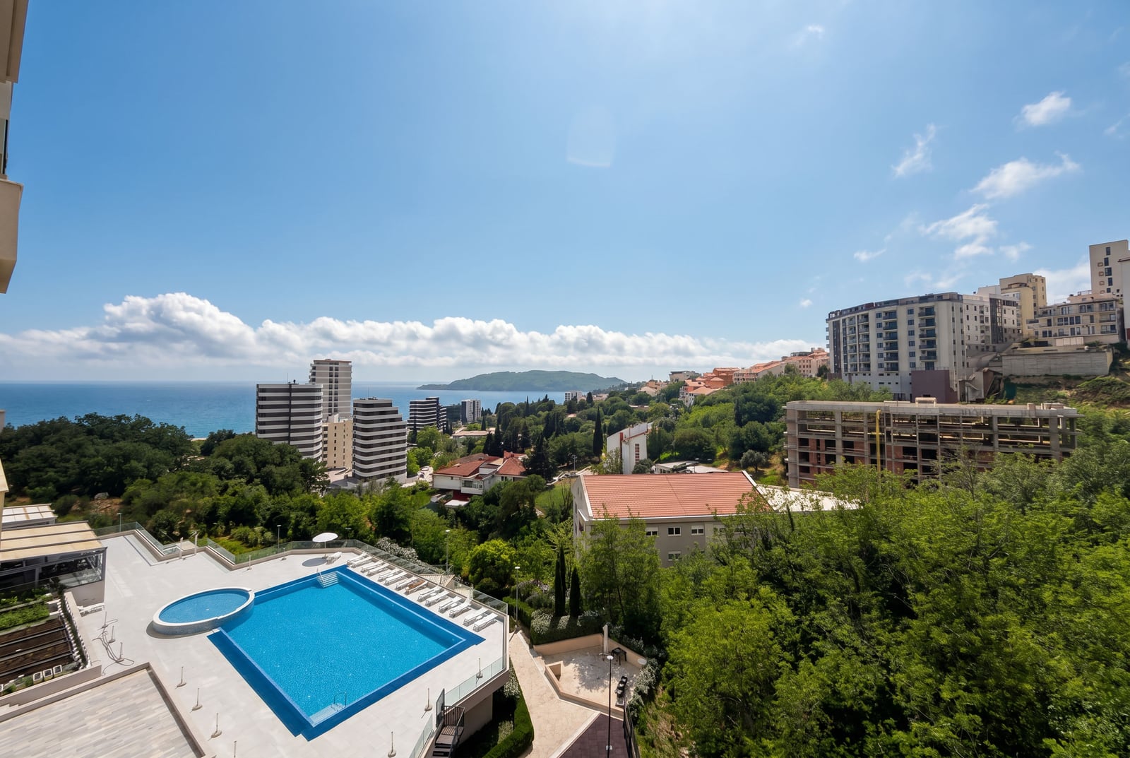 View from the balcony overlooking the outdoor pool, greenery, and the sea in Bečići, Montenegro: a panoramic view of the residential complex with infrastructure.