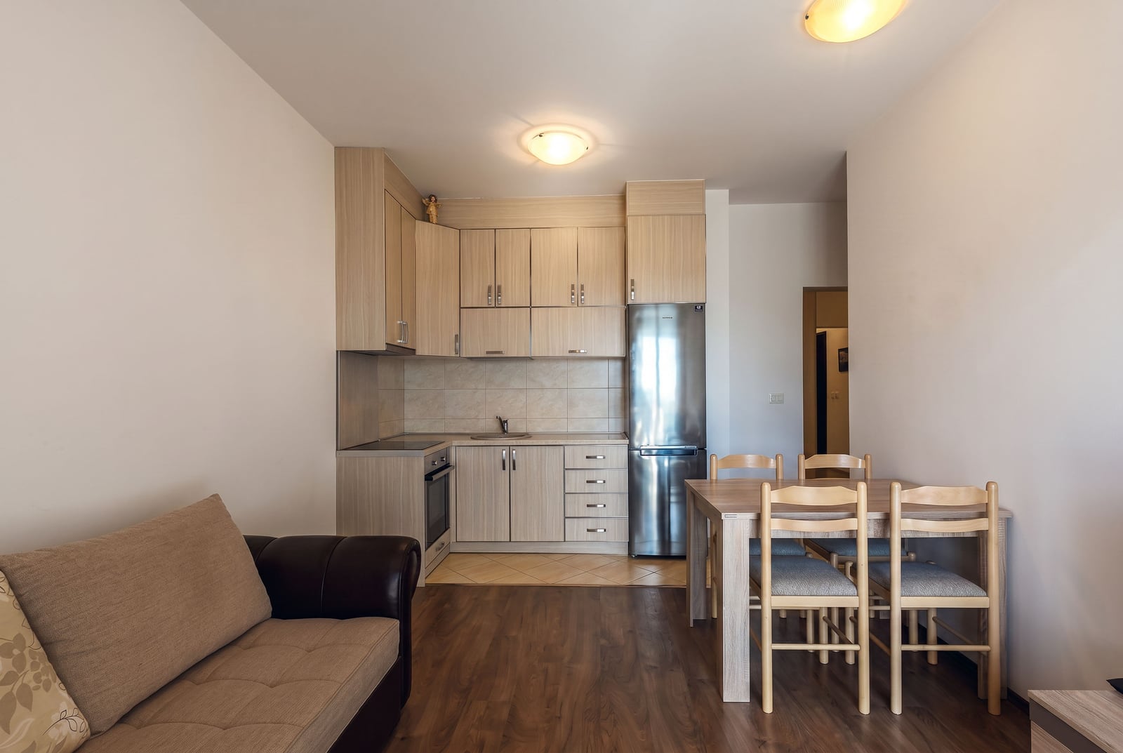Kitchen-living room with dining area in an apartment in Budva, Montenegro: light-colored kitchen set, appliances, and upholstered furniture.