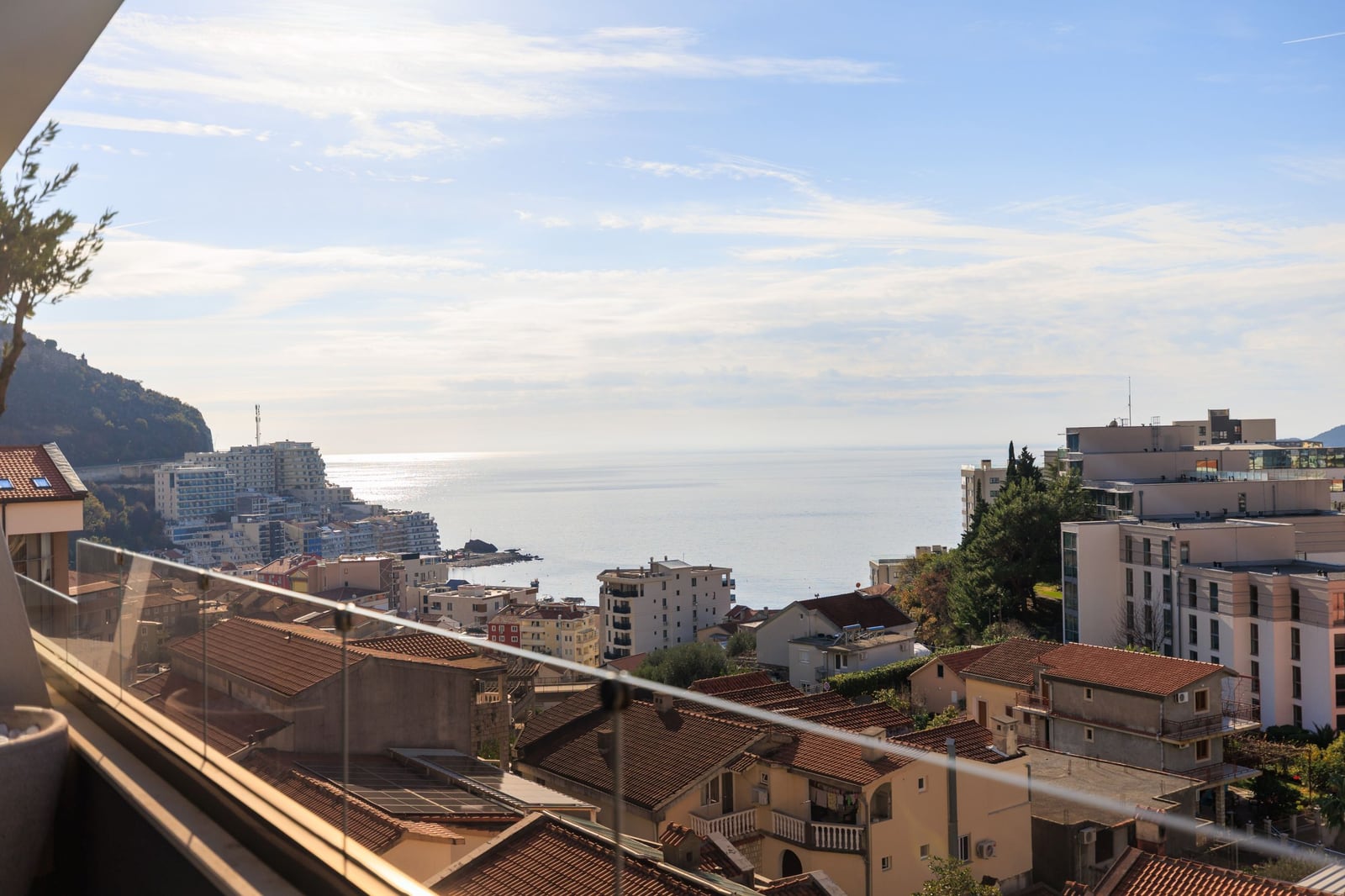 Panoramic sea and Becici town view from a penthouse balcony in Montenegro, glass railing, sunny day.