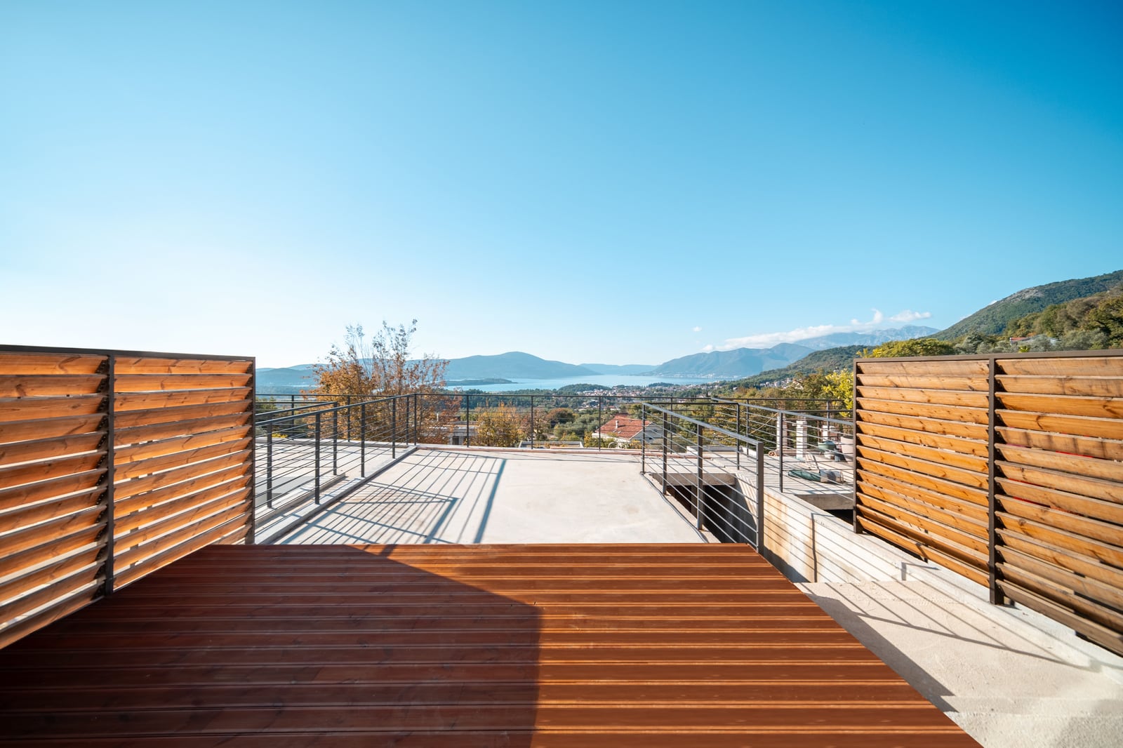 Open terrace of a townhouse in Kavač, Montenegro, with wooden decking, railing, and a panoramic view of the bay.