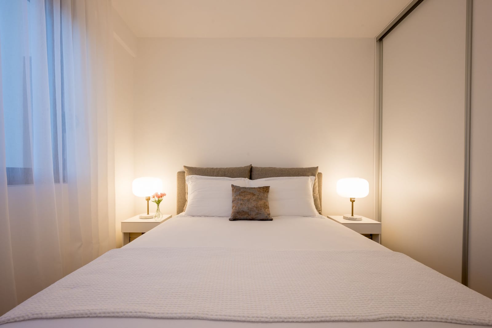 Cozy bedroom with a double bed in a modern apartment in Tivat, Montenegro, featuring white finishes and a sliding-door wardrobe.