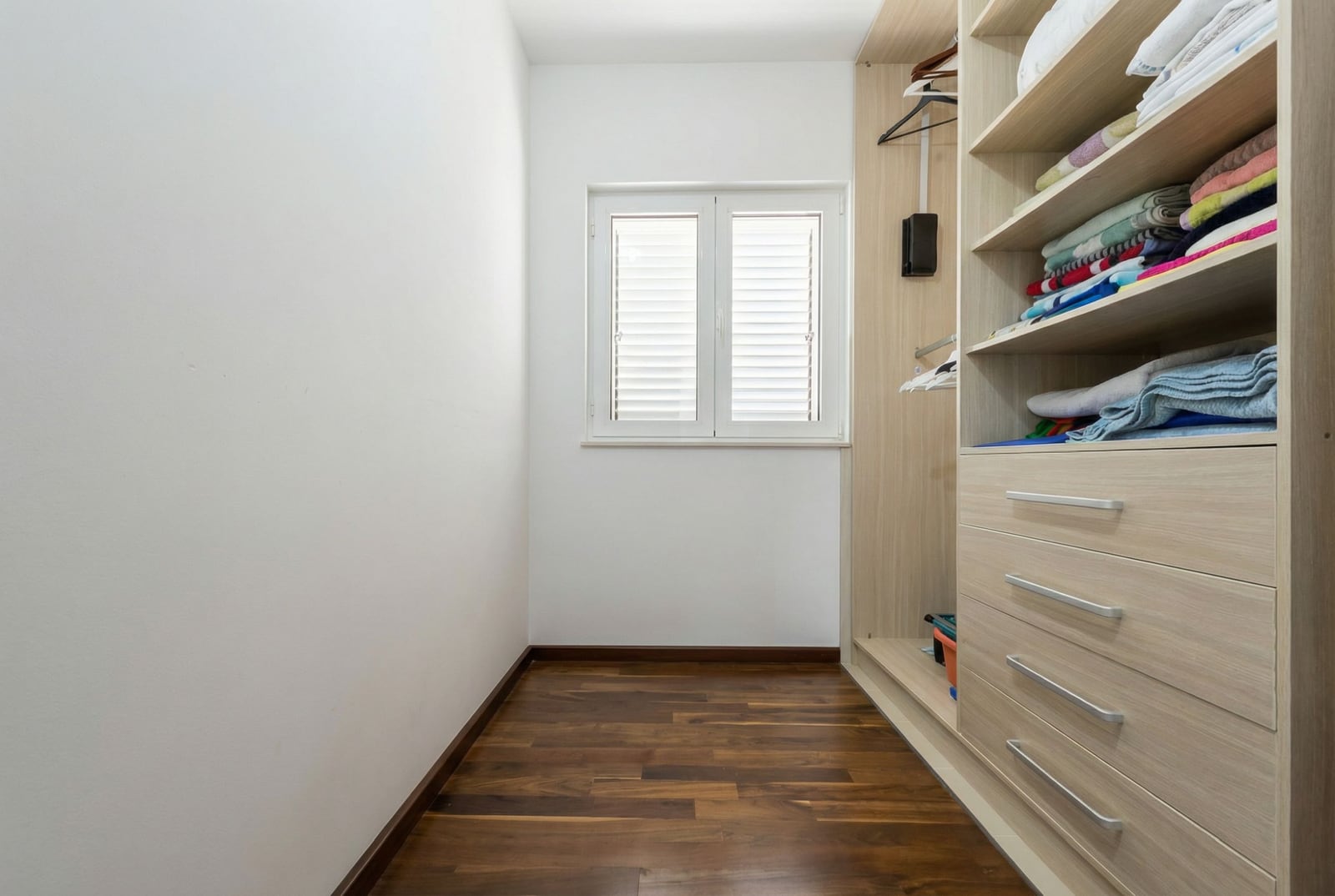 Walk-in closet with a wooden wardrobe and parquet flooring in an apartment in Tivat, Montenegro. Bright room with a window.
