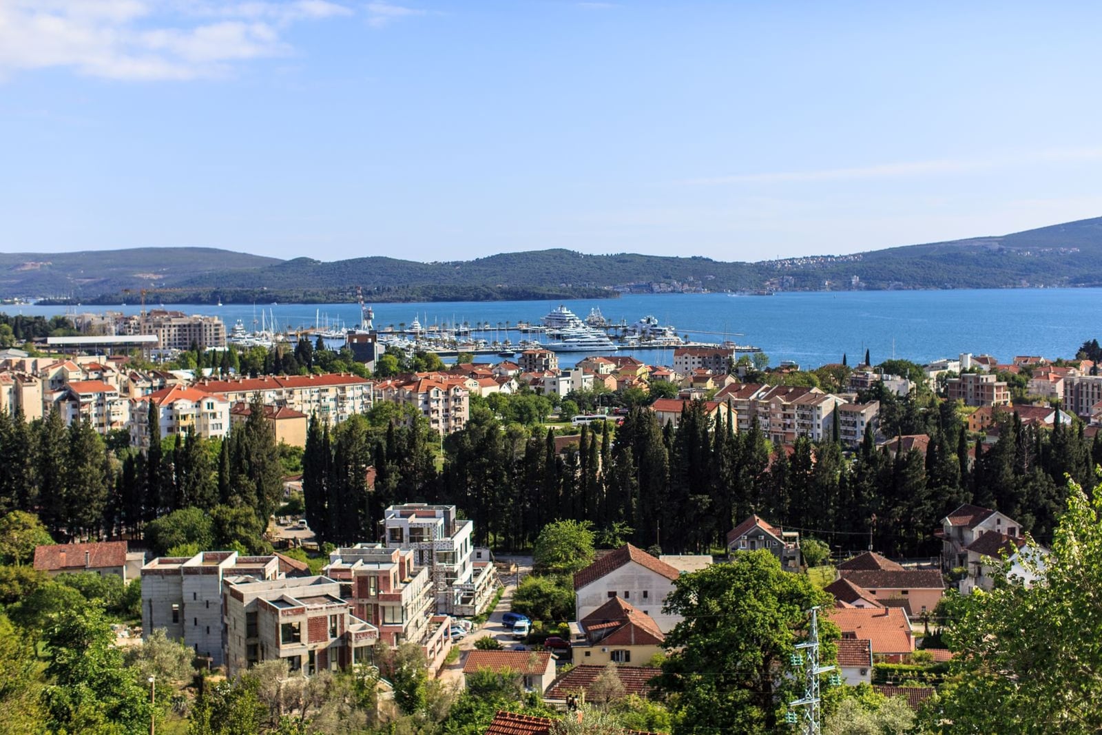 Panoramic view of Tivat and the Porto Montenegro marina in Montenegro, with green hills and the city's residential development.