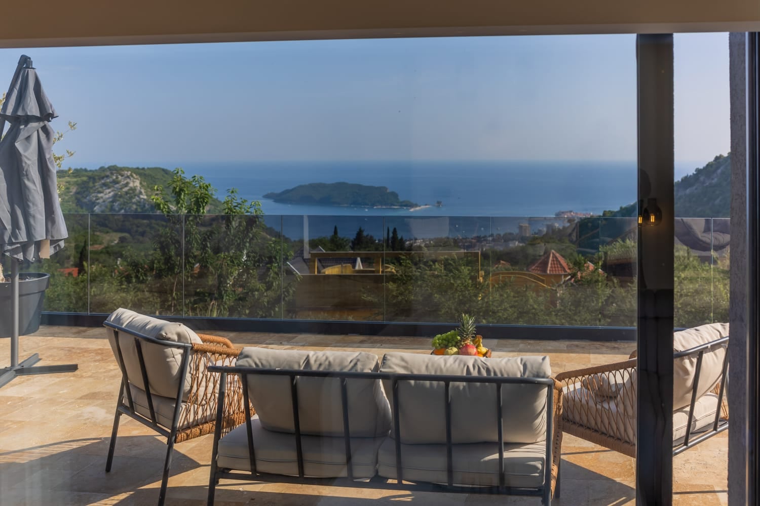 Villa terrace in Budva, Montenegro: wicker furniture, stone floor, and panoramic view of the sea and St. Nicholas Island.