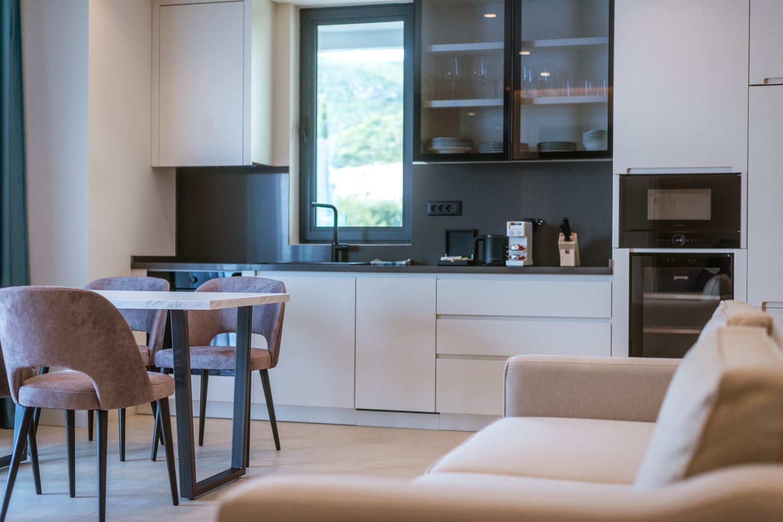 Modern kitchen-living room in an apartment in Bečići, Montenegro: light-colored kitchen set, dining area, and built-in appliances.