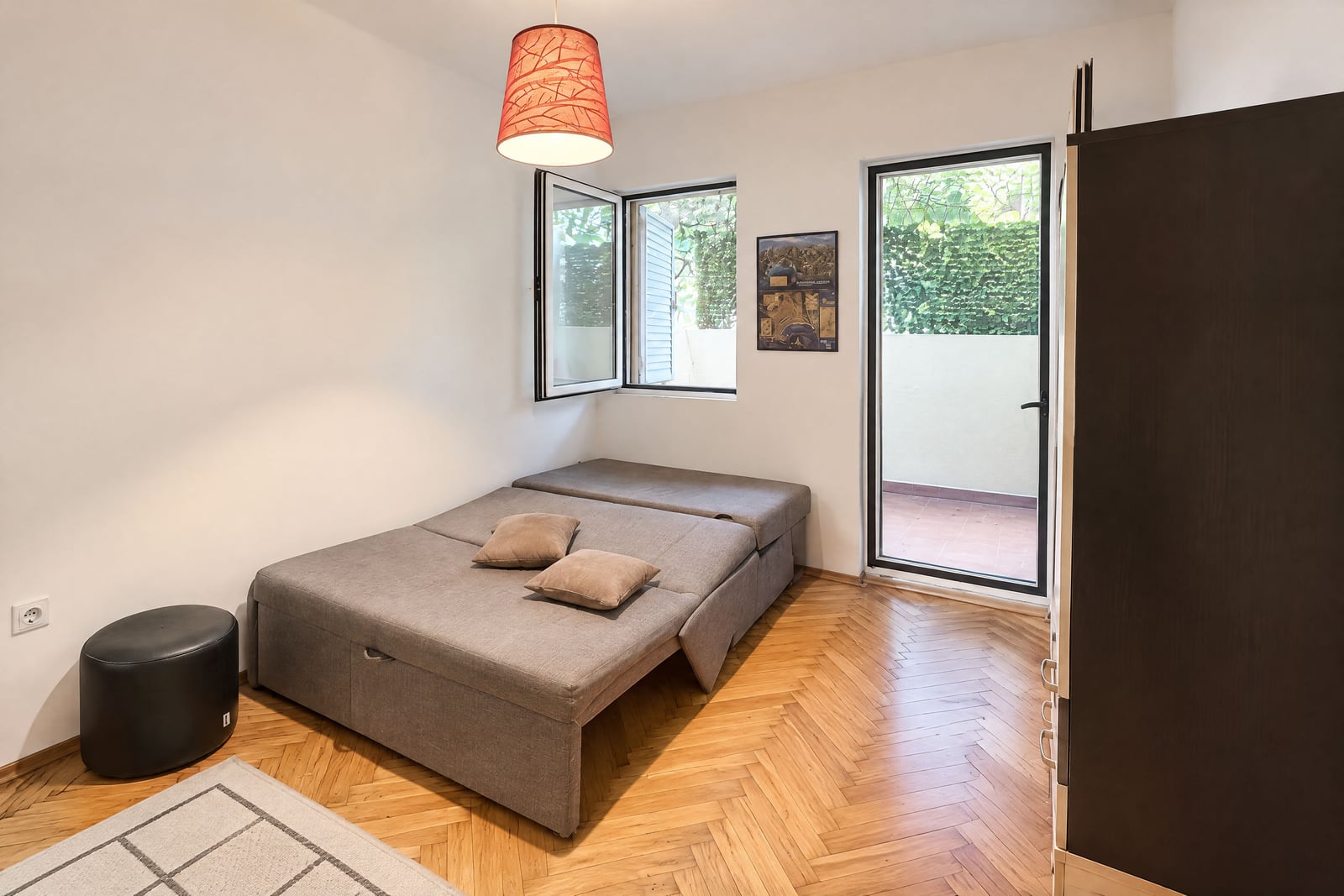 Bedroom featuring a grey sofa bed, wooden parquet flooring, an orange pendant lamp, and a wardrobe.