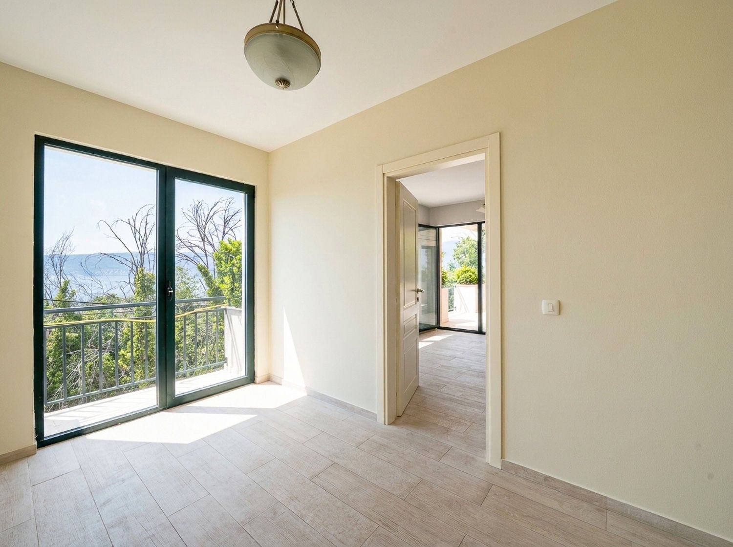 Empty room with light walls, wood-look tile flooring, and a large glass door leading to a balcony.