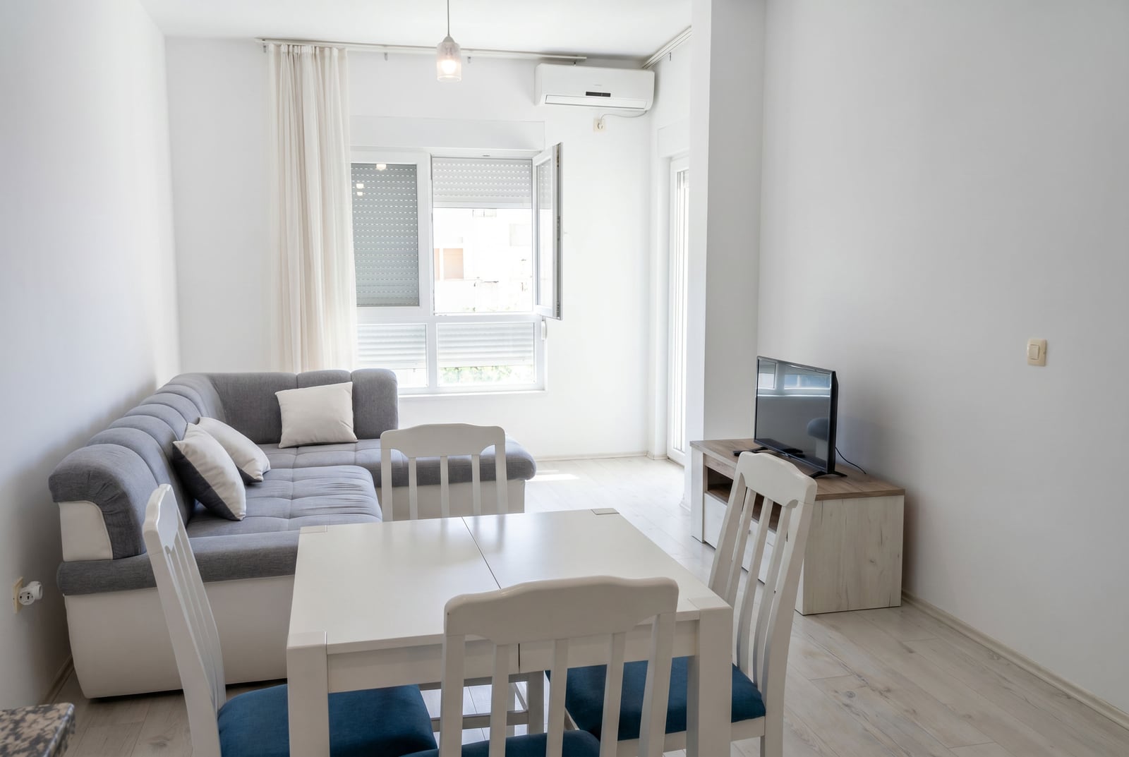 Bright living room with a gray corner sofa and dining area in an apartment in Budva, Montenegro