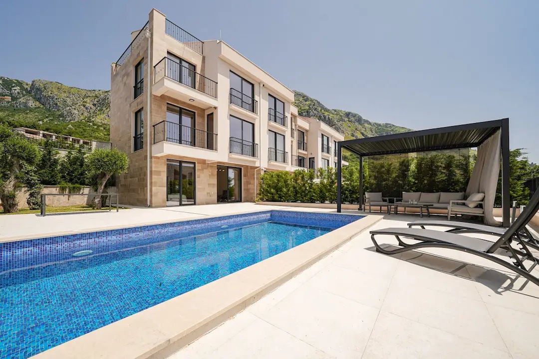 Modern villa in Reževići, Montenegro: outdoor swimming pool, terrace with sun loungers, pergola, and mountain view.