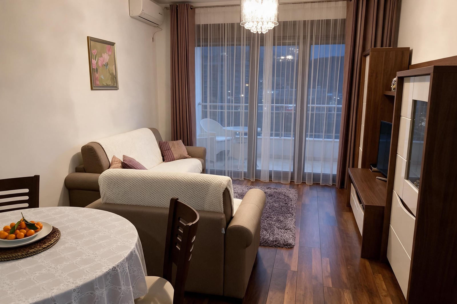 Living room featuring a sofa, dining table with fruit, TV unit, wooden floors, and balcony access.