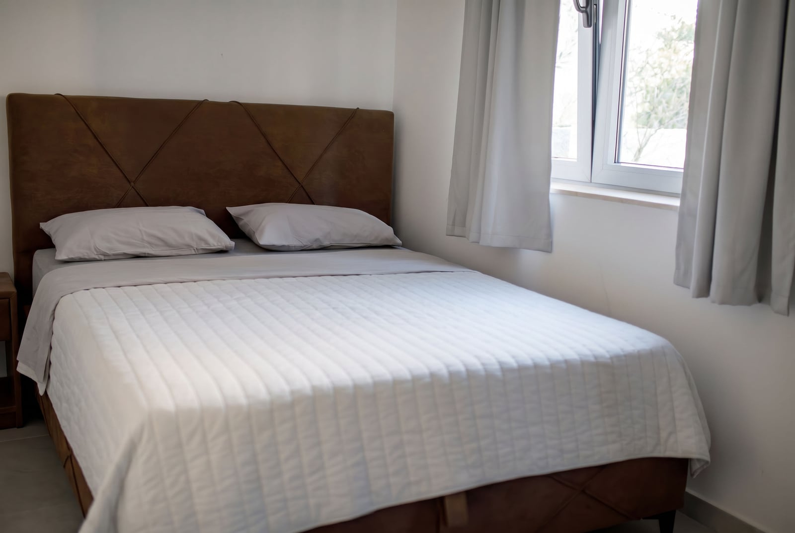 Cozy bedroom with a double bed in an apartment in Risan, Montenegro: modern interior, light tones, and a window.