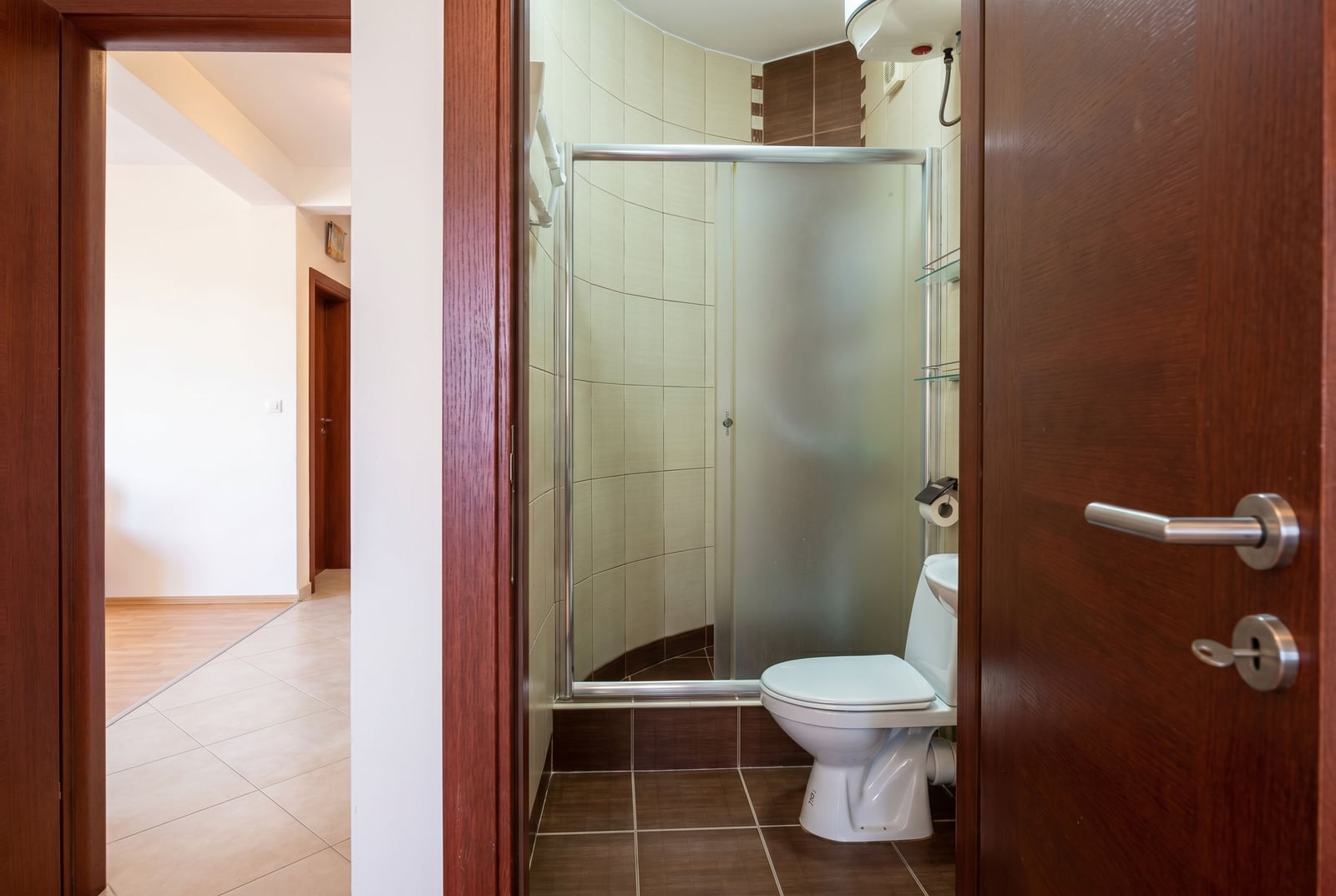 Bathroom with a shower cabin and light-colored tiles in an apartment in Bar, Montenegro. View of the bathroom from the hallway.