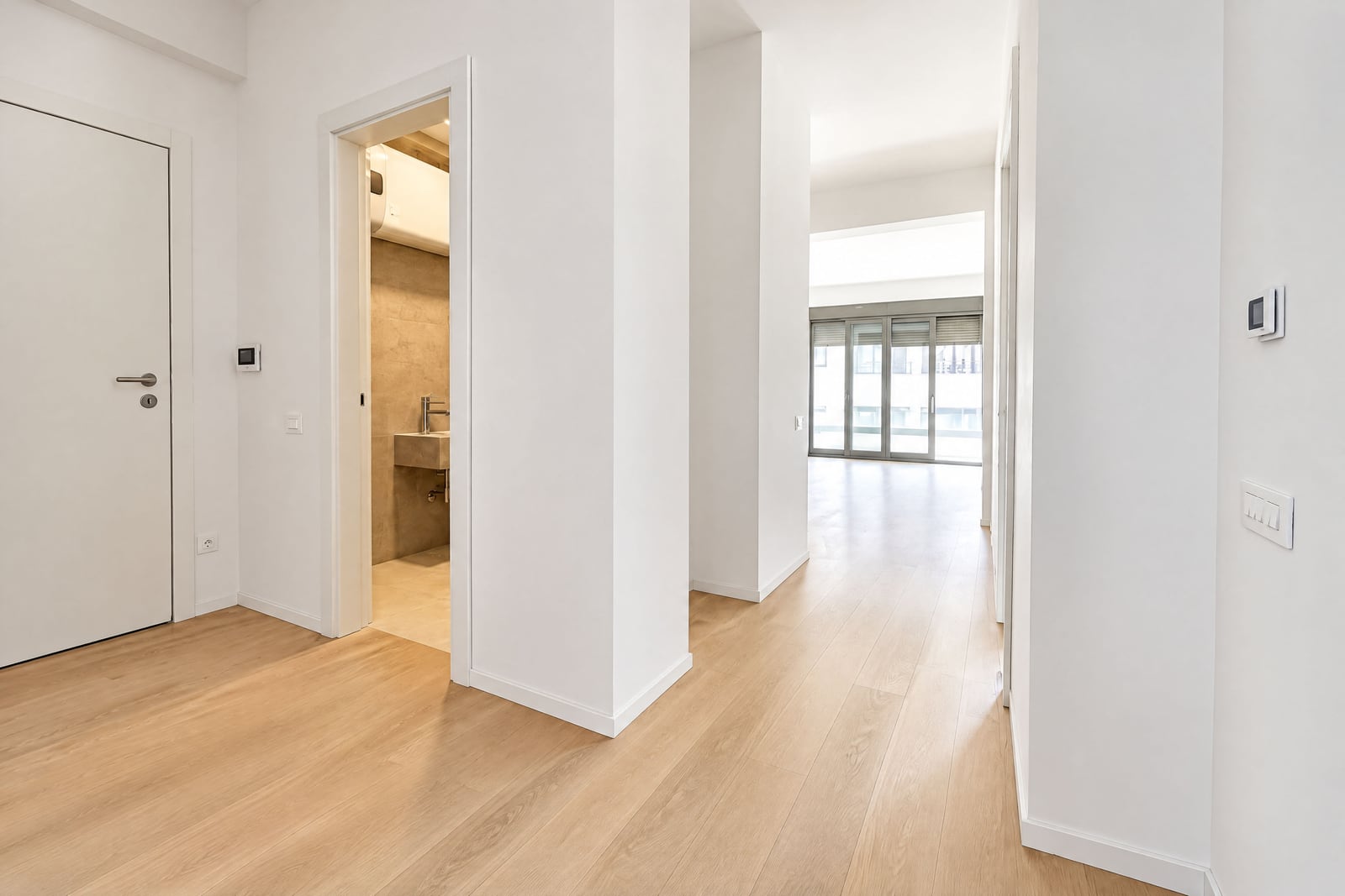 Bright hallway with light wood flooring, an entry door, and a partial view into a bathroom.