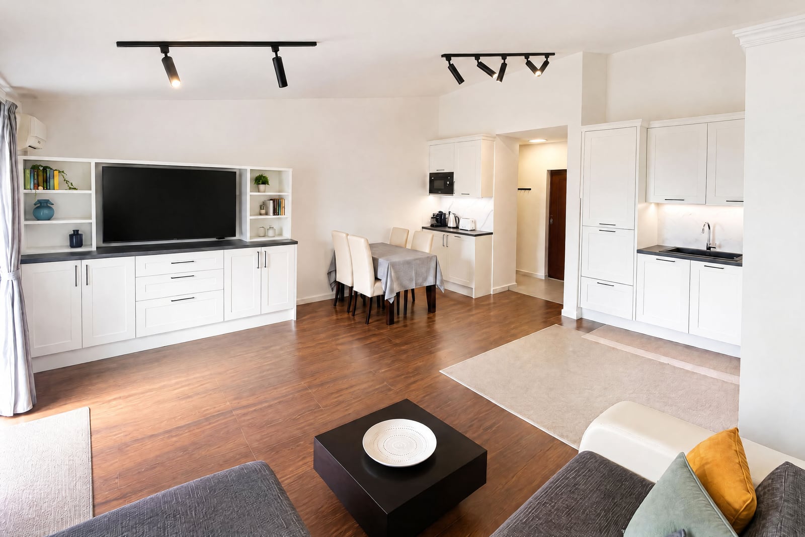 Living room with sofa, TV unit, dining area, and open kitchen on wood floors.