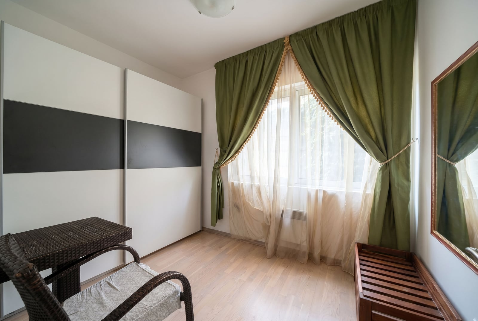 Bedroom in a Kumbor apartment, Montenegro: a bright room with a white sliding-door wardrobe, wicker furniture, and green curtains.