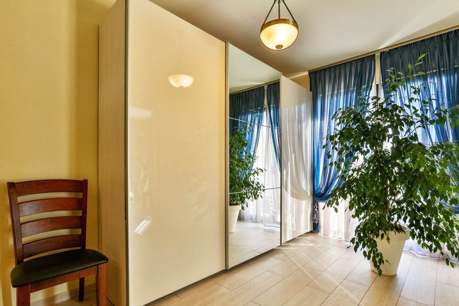 Bedroom in a villa in Tivat, Montenegro: glossy wardrobe with a mirror, wooden chair, and indoor plant by the window.