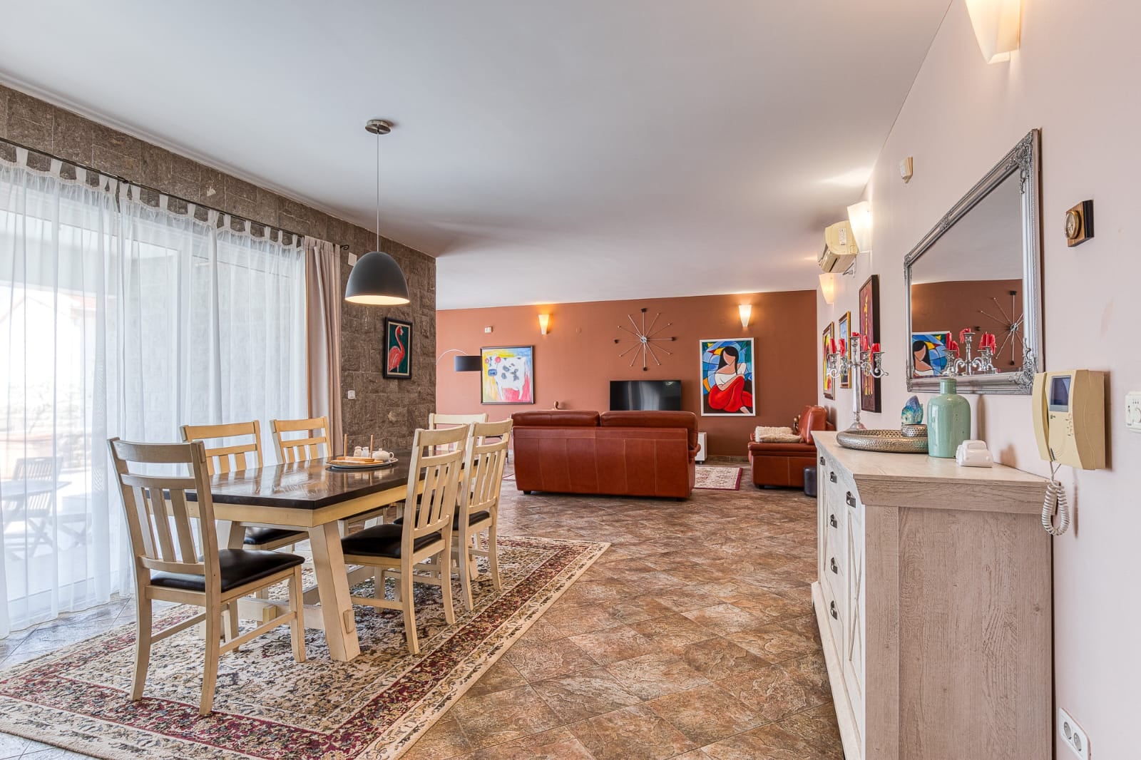 Spacious living room with a dining area in a villa in Becici, Montenegro: leather furniture, stone finishes, and panoramic windows.