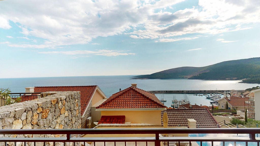 View from the balcony overlooking the sea, the yacht marina, and the tiled roofs of houses in the Luštica Bay residential complex, Montenegro.