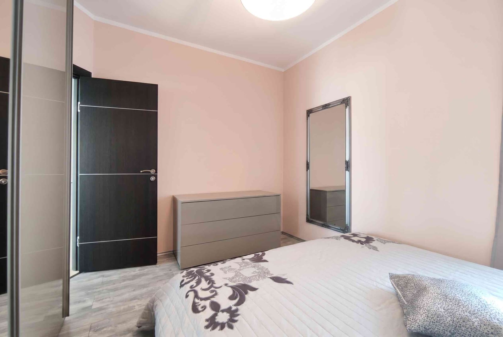 Bright bedroom in an apartment, Bečići, Montenegro: double bed, dresser, mirror, and dark interior door.