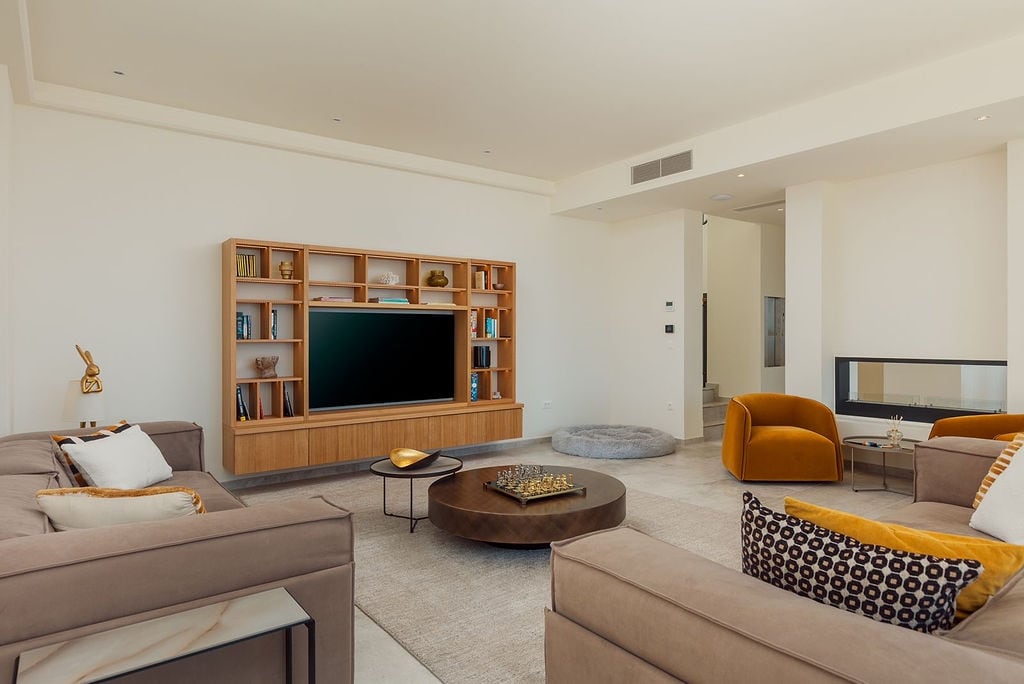 Modern living room with a fireplace and wooden shelving unit in a villa in Luštica, Montenegro. Cozy upholstered furniture in the interior.