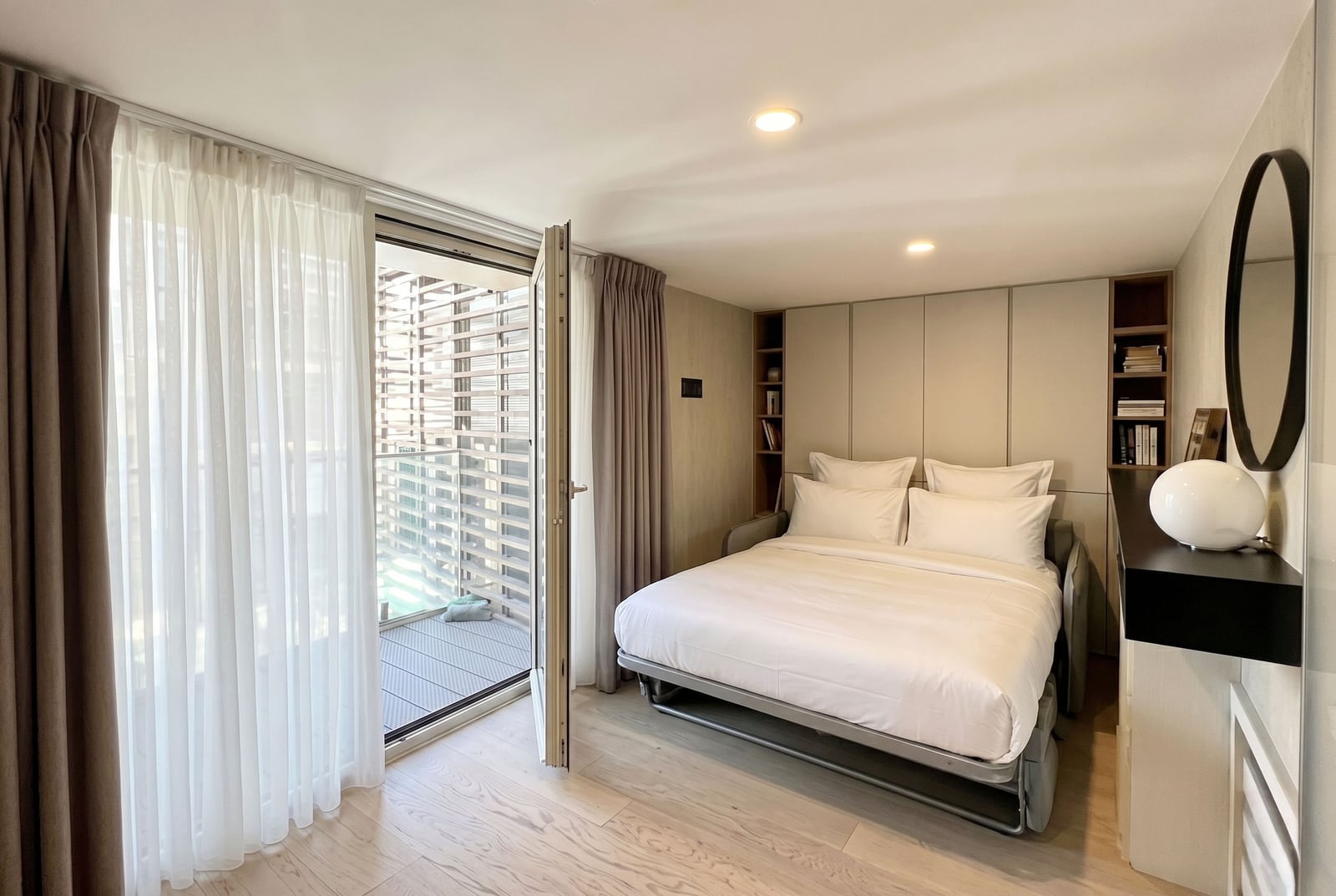 Modern bedroom in a Budva apartment, Montenegro: double bed, built-in shelves, and balcony access.
