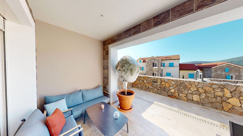 Cozy terrace with upholstered furniture and stone finishes in the Luštica residential complex, Montenegro. View of the mountains and houses.