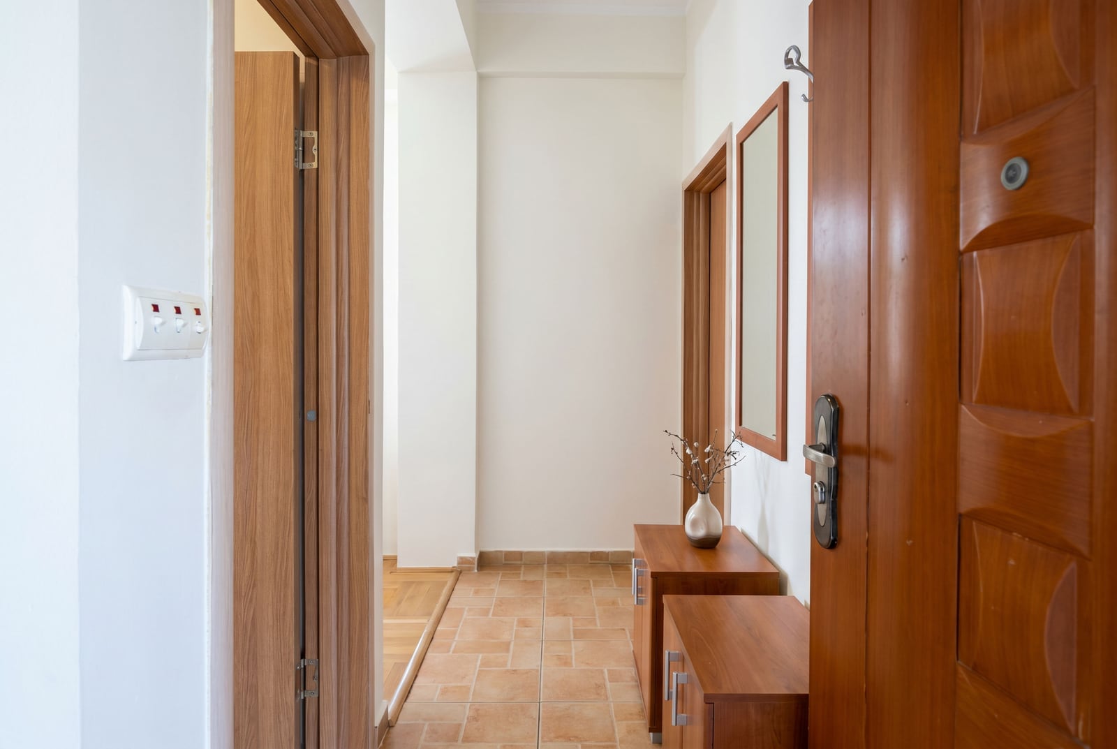 Bright hallway in a Budva apartment, Montenegro: wooden doors, tiled flooring, and a console table with a mirror in the interior.