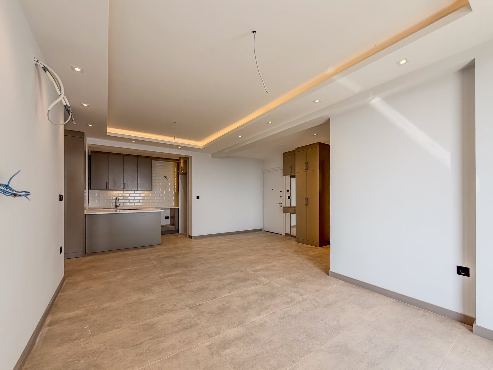 Empty open space with tile floor, visible kitchen island, wooden wardrobe, and exposed wiring on the wall.