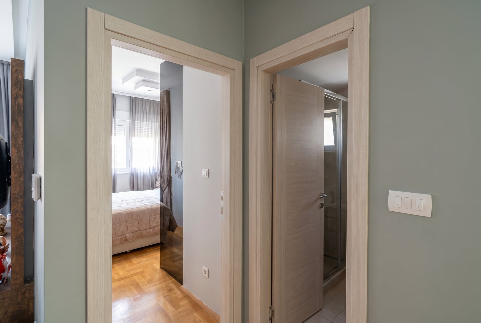 Interior of an apartment in Budva, Montenegro: view from the hallway into the bedroom with parquet flooring and the bathroom with a walk-in shower.