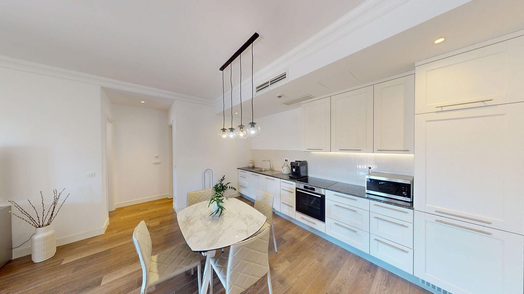 Modern kitchen-dining room with white cabinetry and a marble table in an apartment, Luštica, Montenegro.