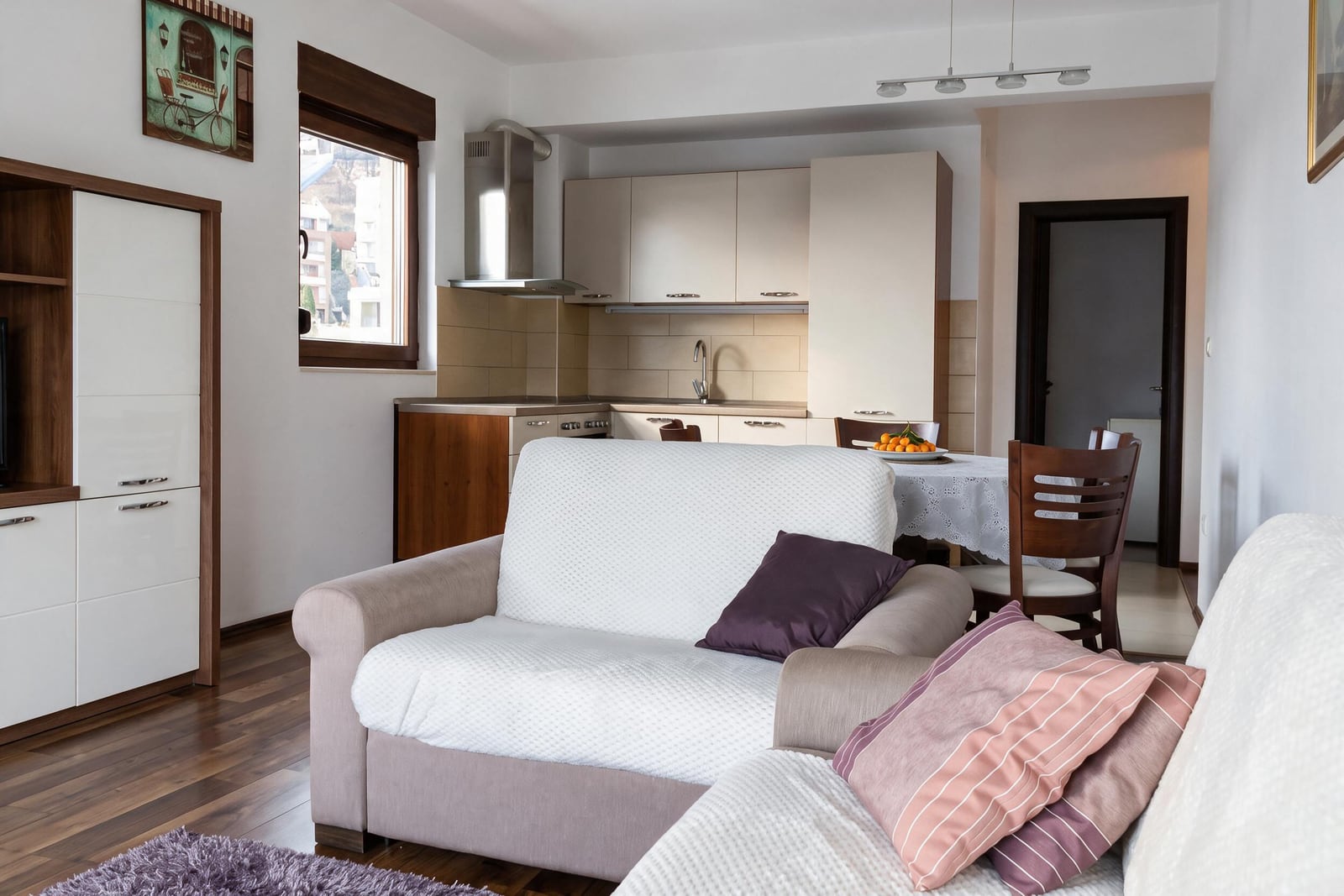 Living room with beige sofa and open kitchen area in background, featuring wood floors.