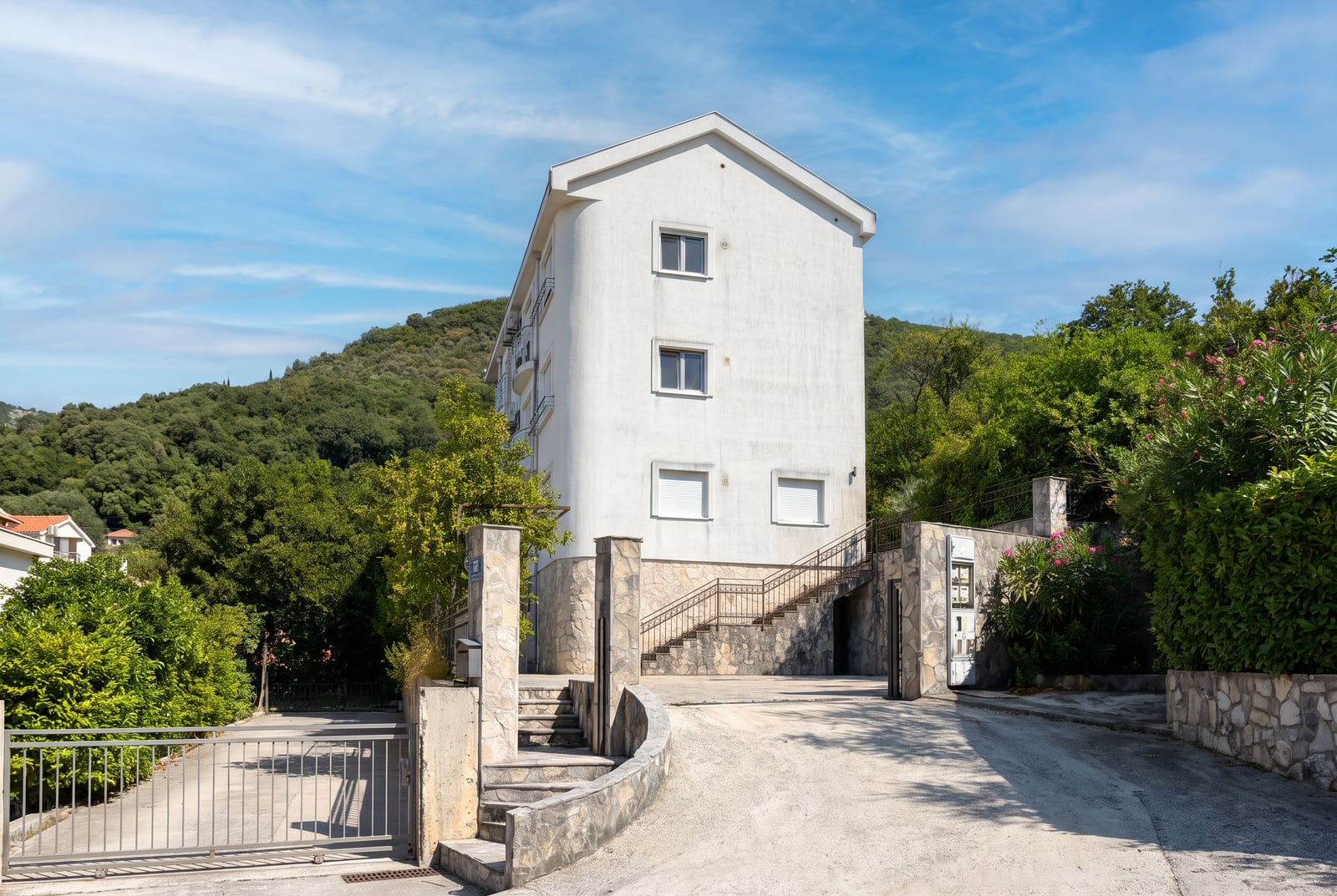 White three-story residential building with stone cladding and green area in Tivat, Montenegro