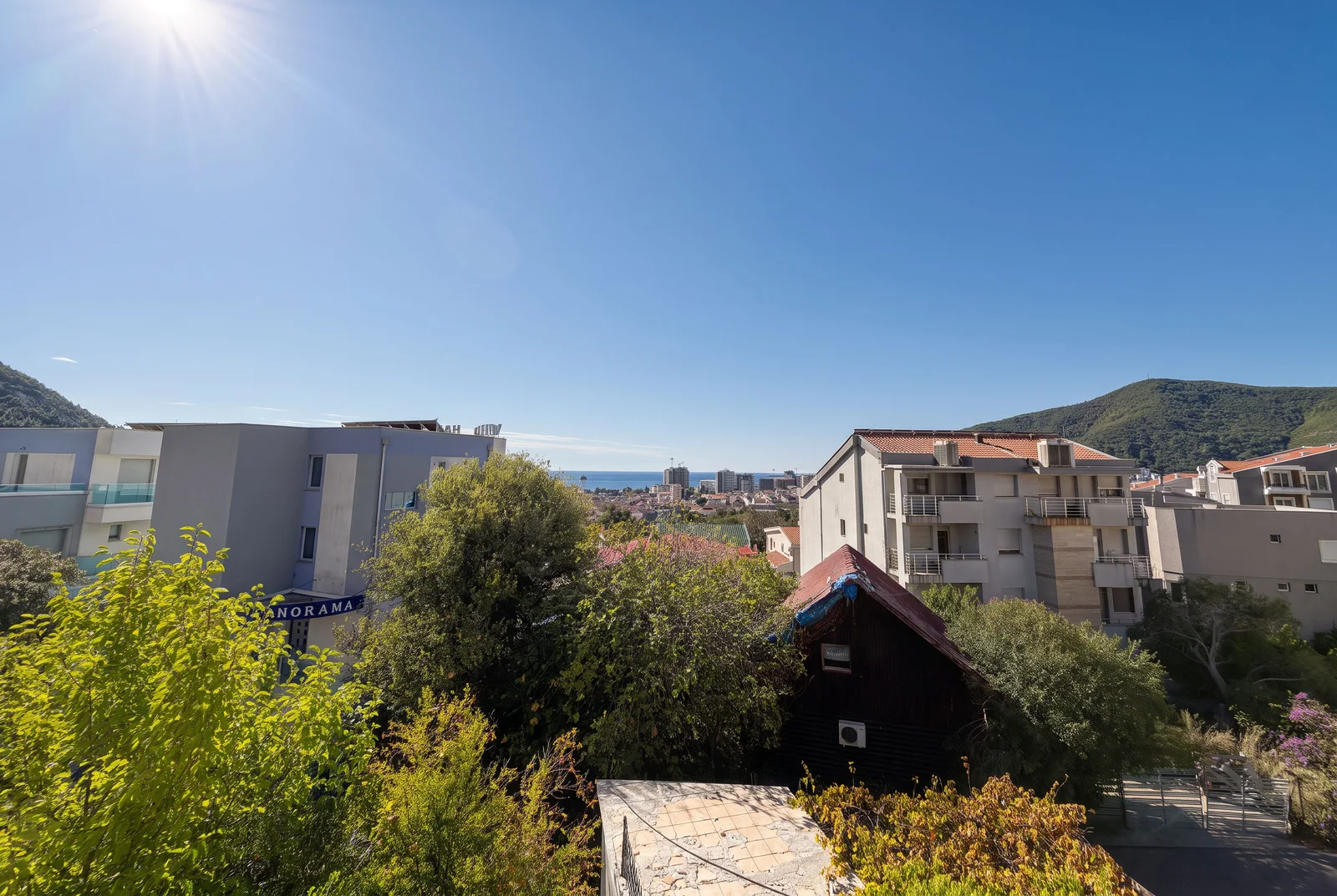 Panoramic view of the city, sea, and mountains from a terrace on a sunny day.